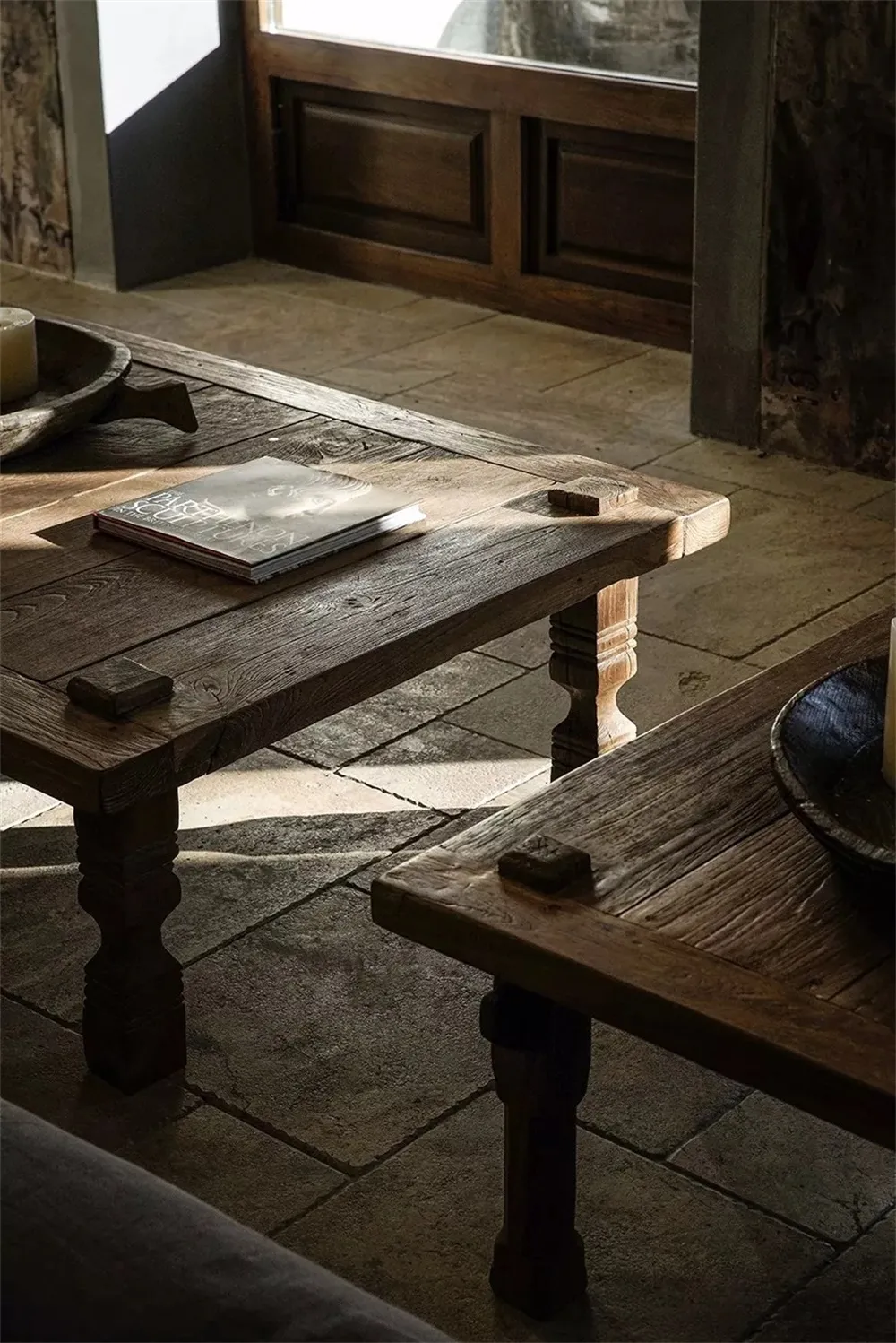 Wooden tables in an industrial-style living room with natural light and exposed stone walls.