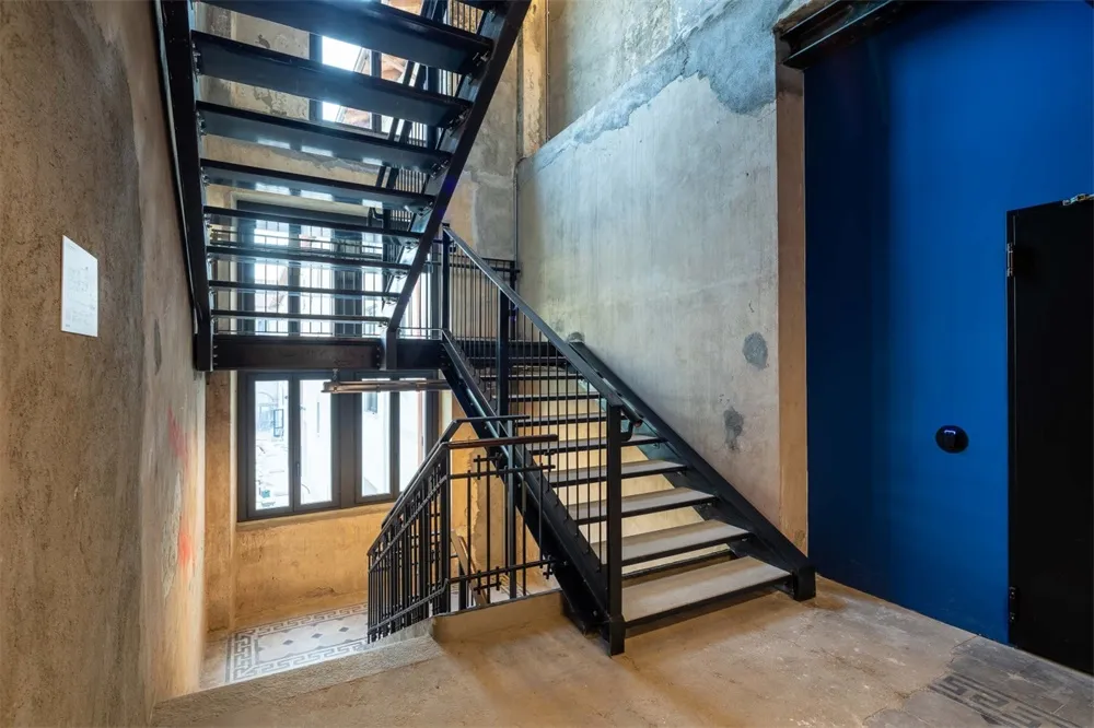 Industrial-style metal staircase indoors with concrete flooring and a blue door.