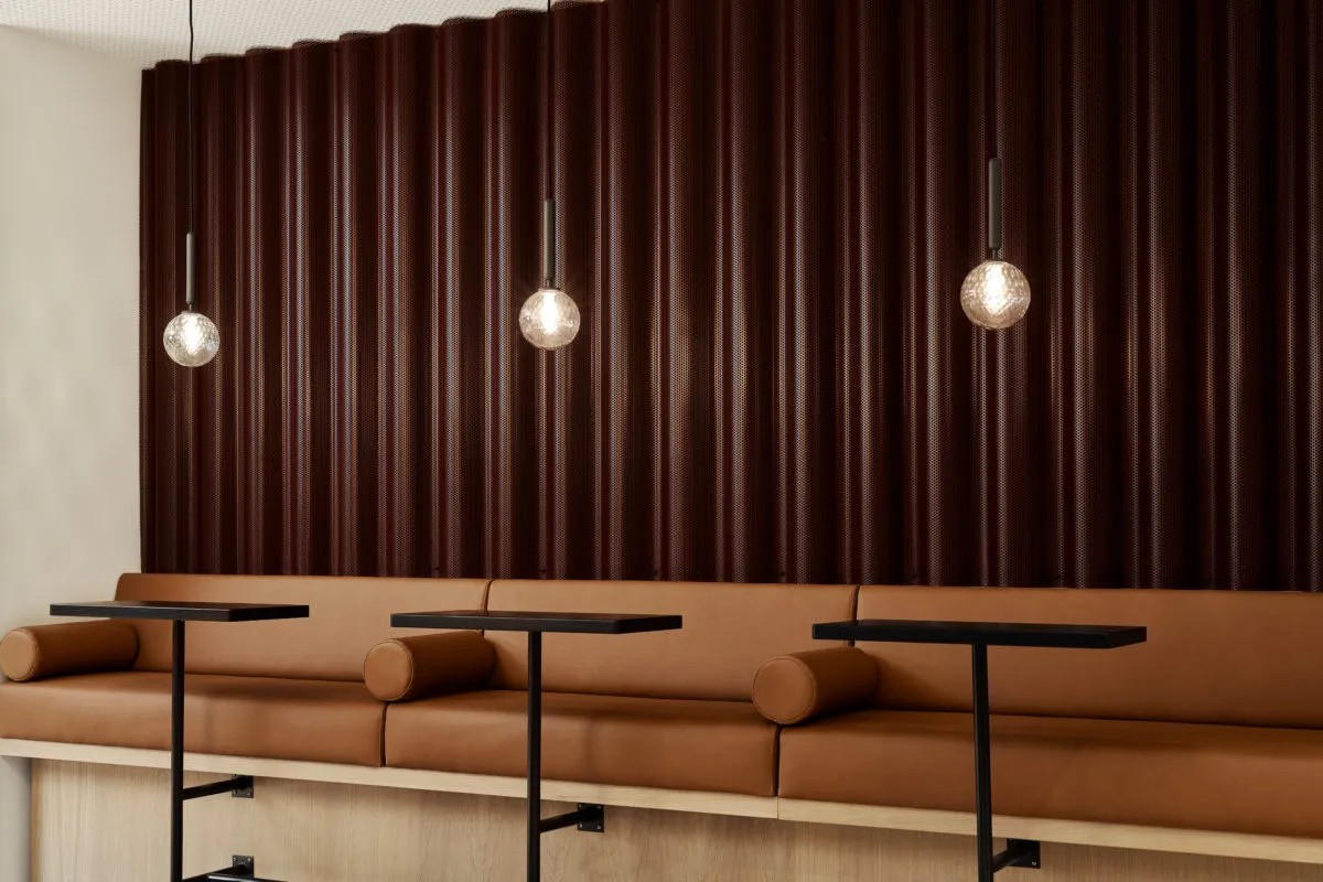 Modern bar seating with brown leather upholstery, pendant lights above, and a textured dark-colored wall.