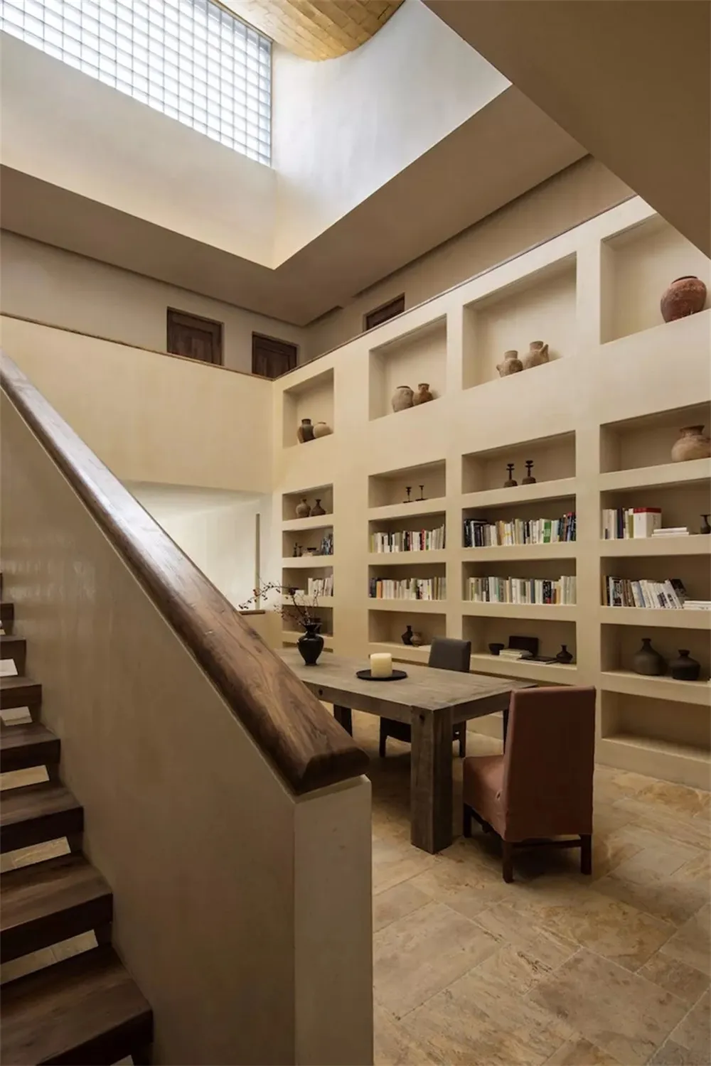A modern library with concrete shelving and a wooden table surrounded by chairs.