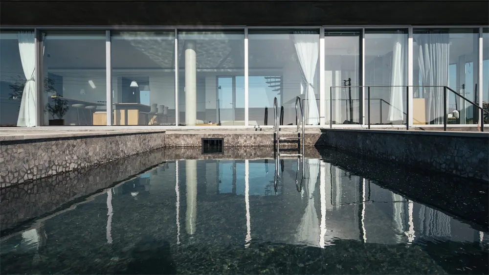 Modern residential swimming pool with concrete edges and glass walls.
