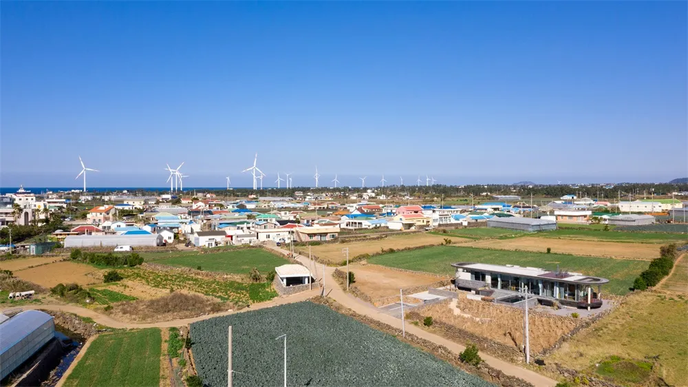 從空中俯瞰一座小鎮,背景有風力發電機,代表永續能源發展。