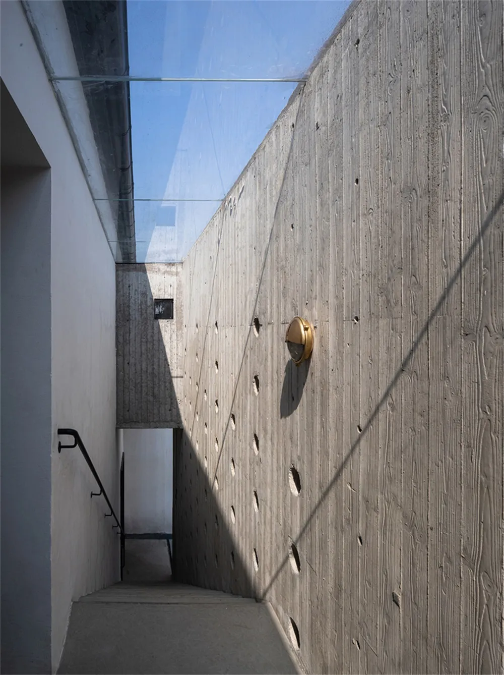極簡建築室內,混凝土牆搭配金色燈具與玻璃天花板。