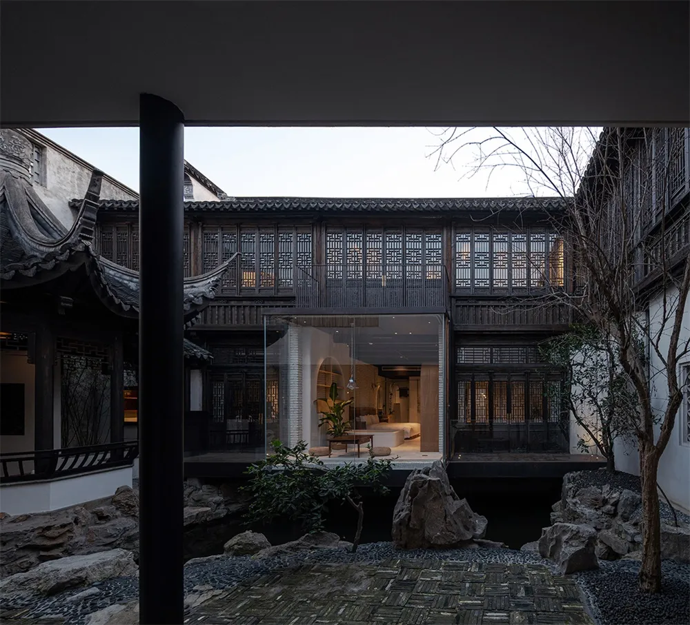 A traditional Chinese garden with wooden beams, glass seating, and stone path.