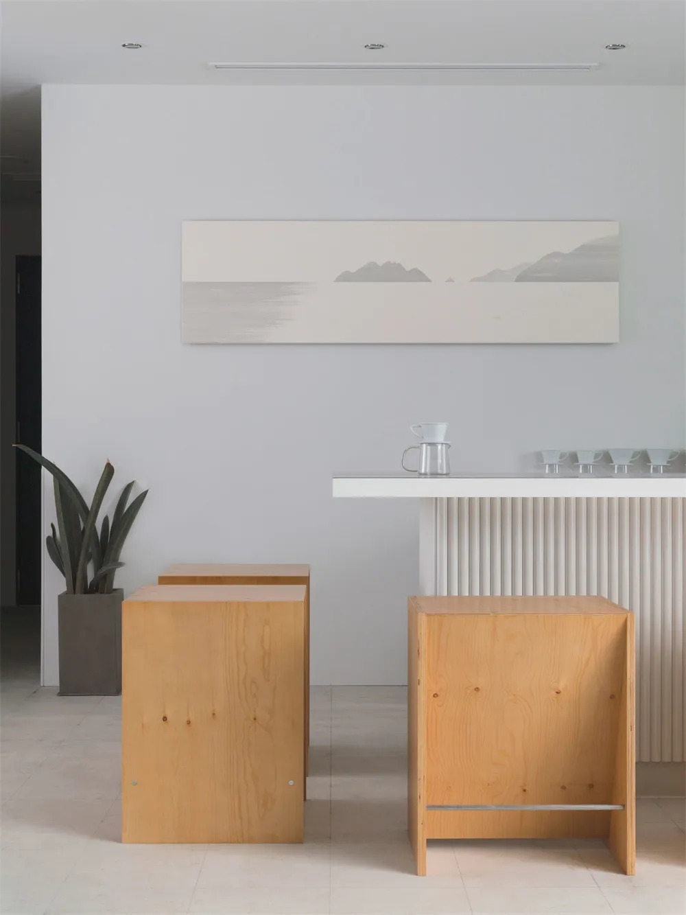 Minimalist design featuring wooden stools, a white counter, and a serene seascape painting.
