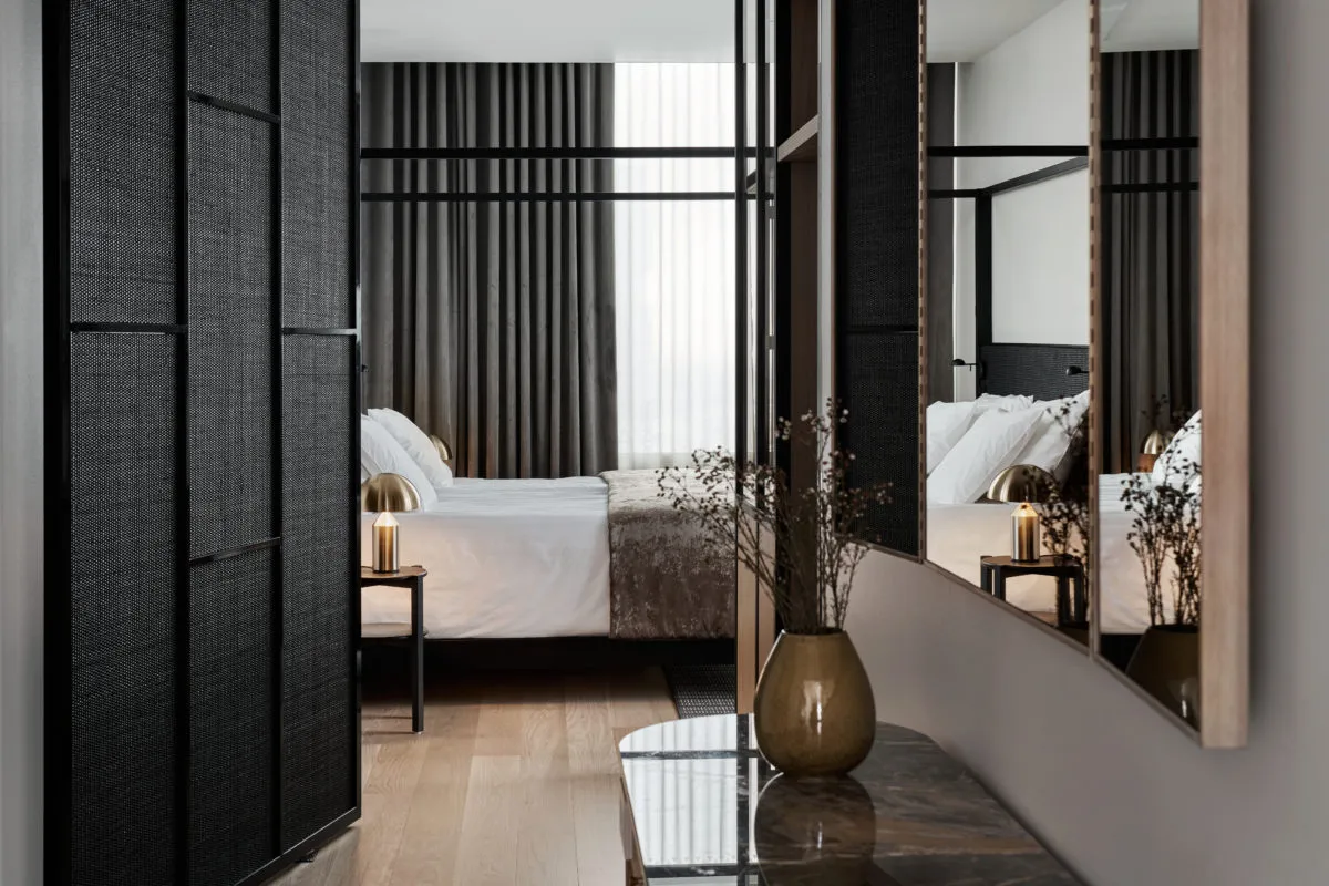 A minimalist bedroom featuring fabric bedding, a wooden floor, and metallic accents.