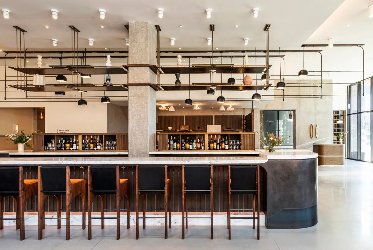 Modern industrial bar with marble countertops, metal stools, and a concrete pillar.