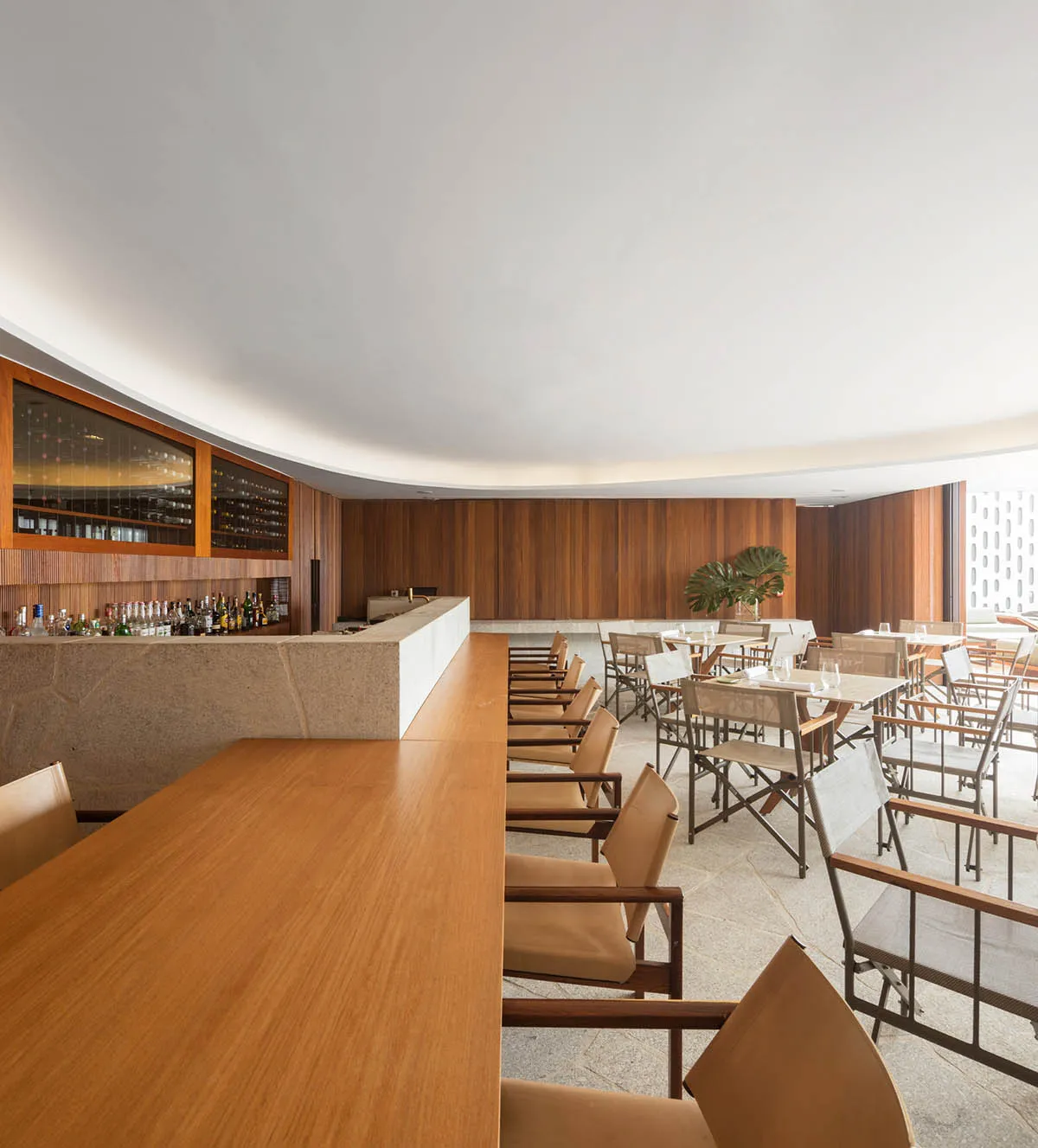 An elegant restaurant bar with wooden chairs, marble countertops, and a curved wooden wall.