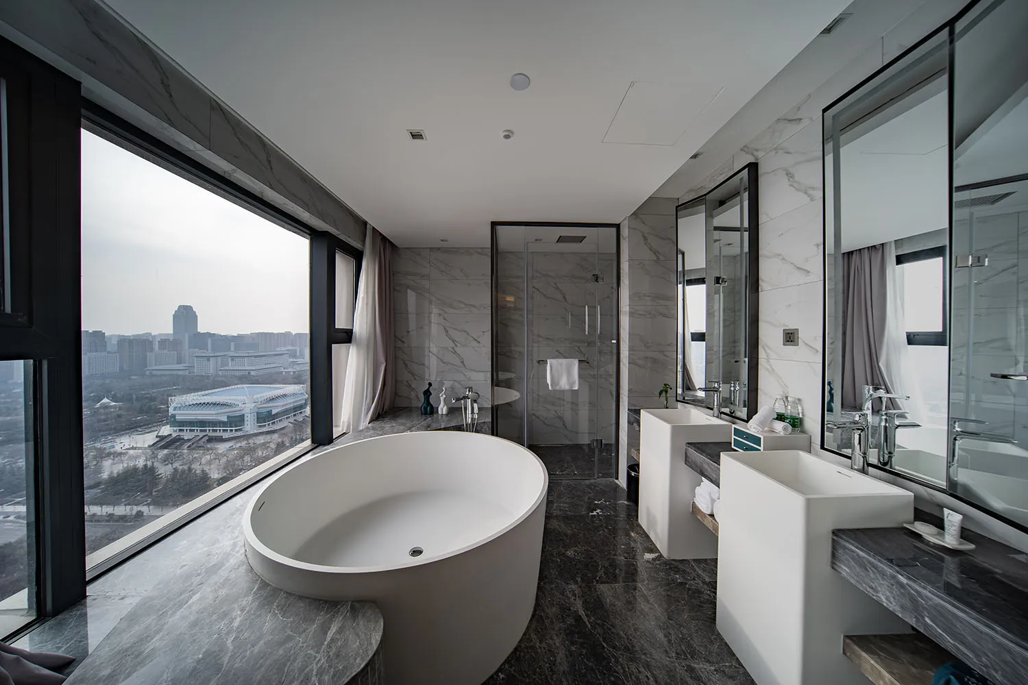 Modern bathroom featuring a freestanding bathtub with a cityscape view through large windows and marble flooring.