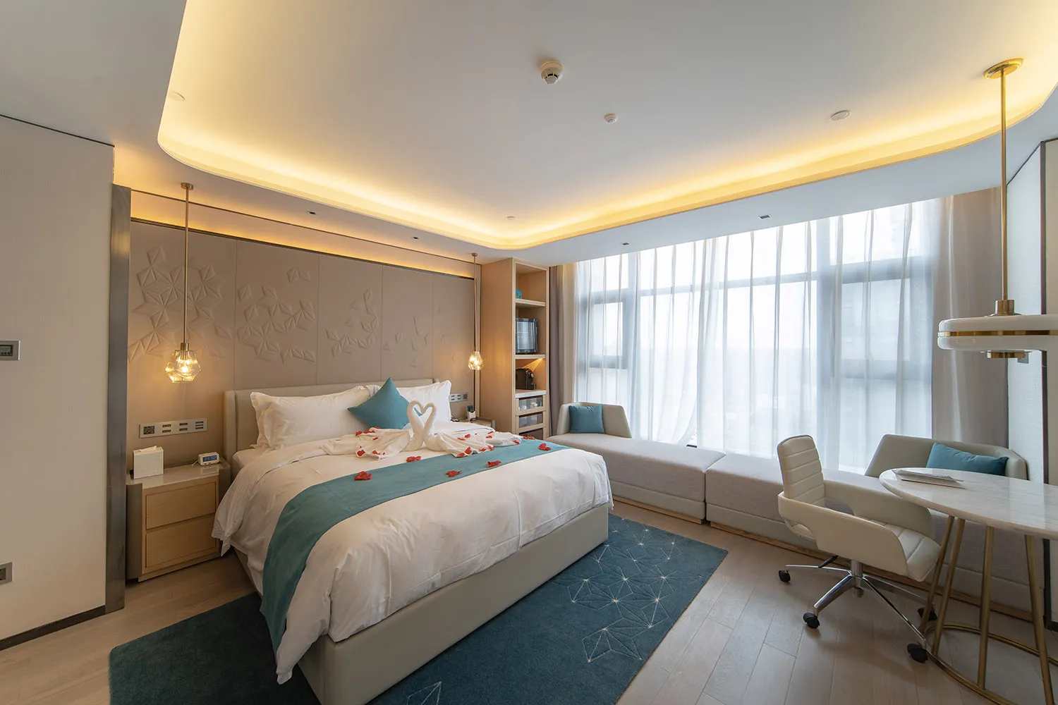 Modern bedroom suite with white and blue decor, featuring a bed, couch, desk, and large windows.