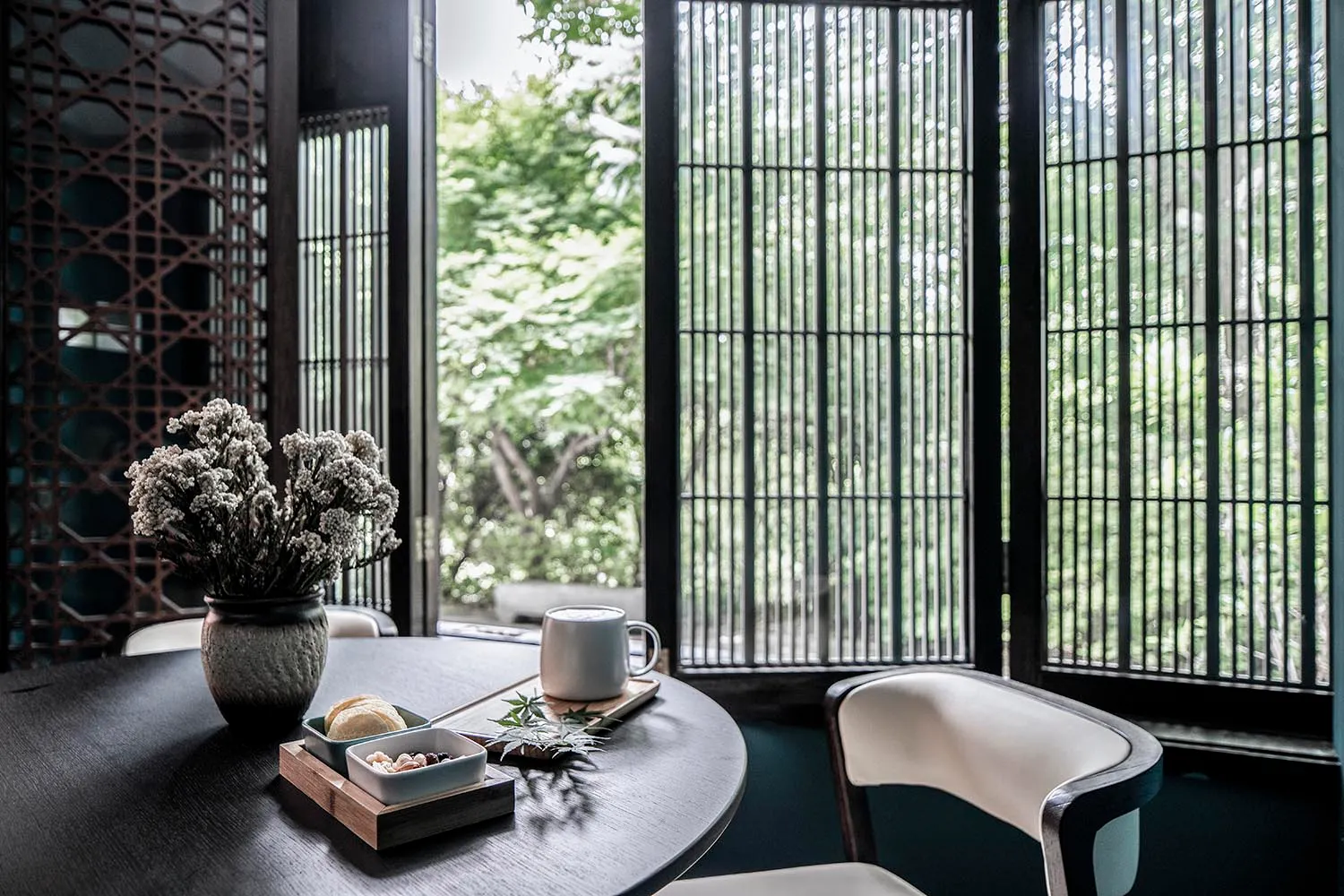 A cozy coffee shop with a wooden table, white chairs, and a vase of flowers.