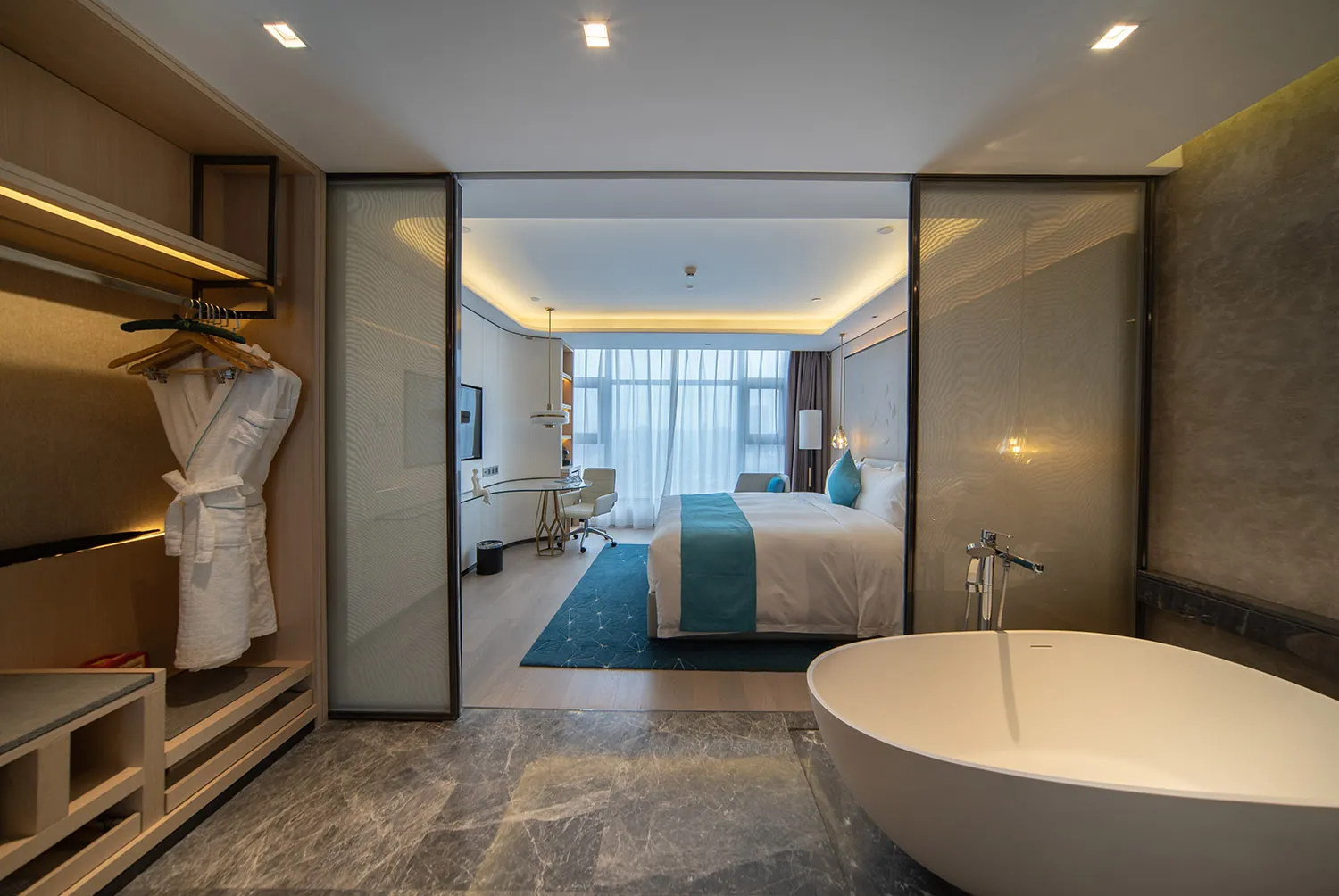 Modern hotel suite featuring a marble bathroom and bedroom area with a large bathtub and white furniture.