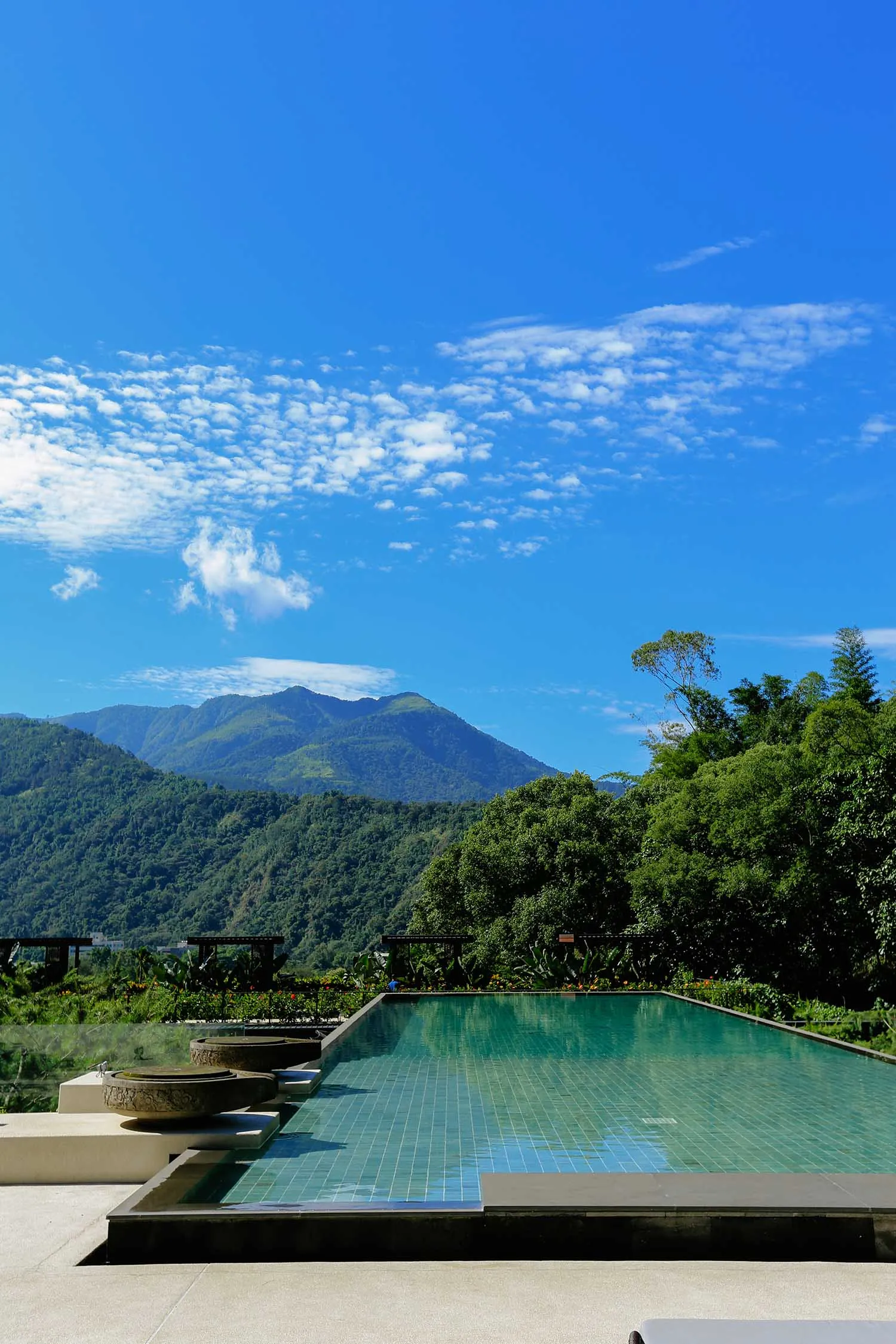 A serene pool surrounded by lush greenery with a mountain landscape in the background.