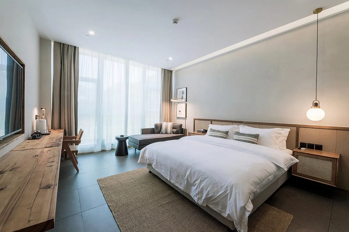 Modern bedroom with white textured fabric, minimalist design, and large glass windows.