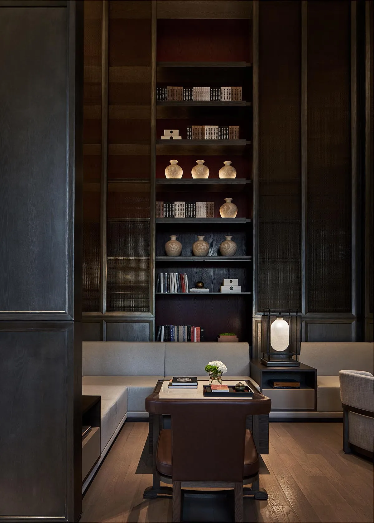 A minimalist library with a wooden shelving unit displaying books and decorative vases, featuring a leather sofa and marble c