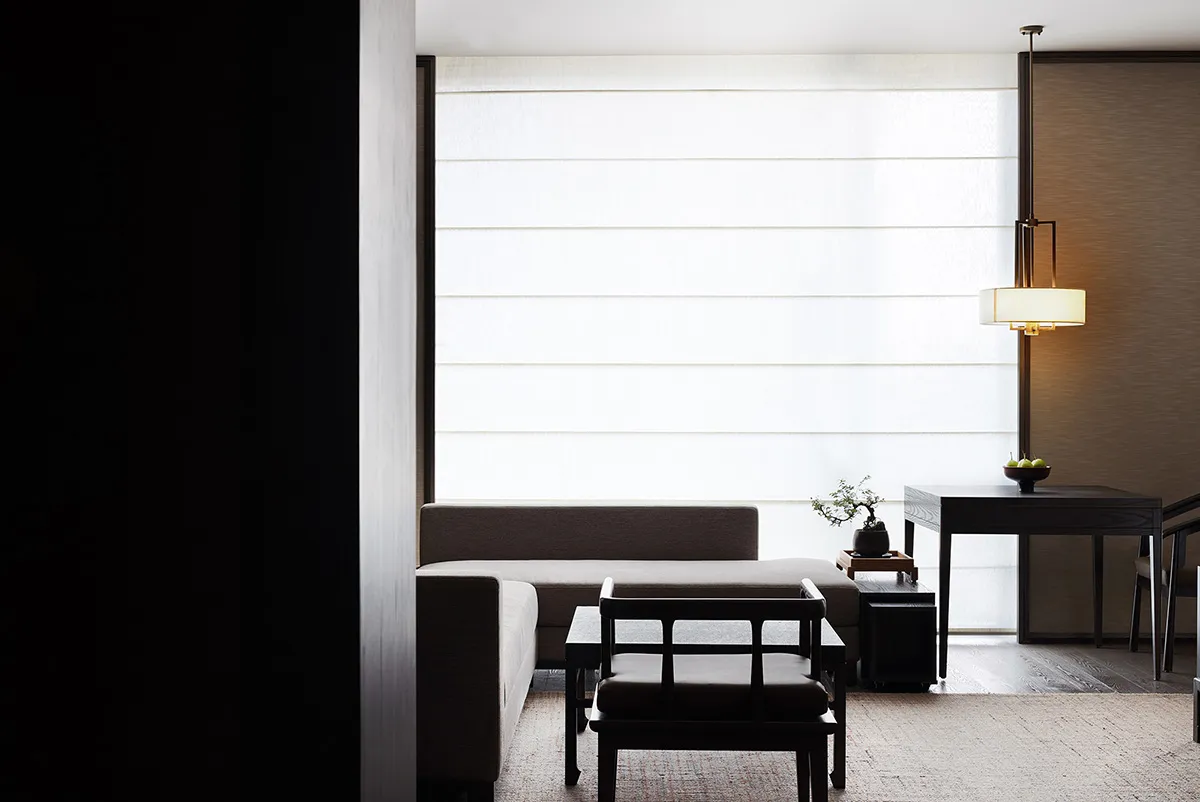 A minimalist living room with a neutral-toned sofa, table, and chairs under a lit hanging lamp.