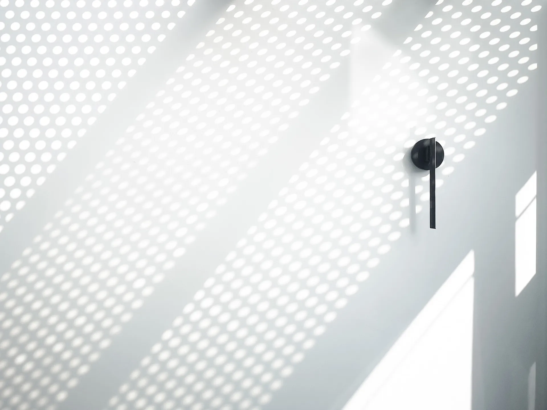 Perforated metal wall with light shining through, creating a minimalist design aesthetic.