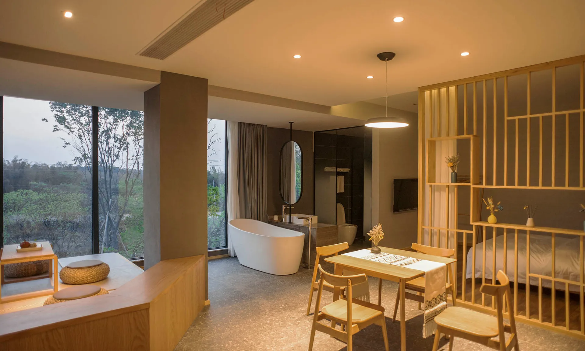 Spacious minimalist residential bathroom with a freestanding bathtub, wooden furniture, and stone flooring.