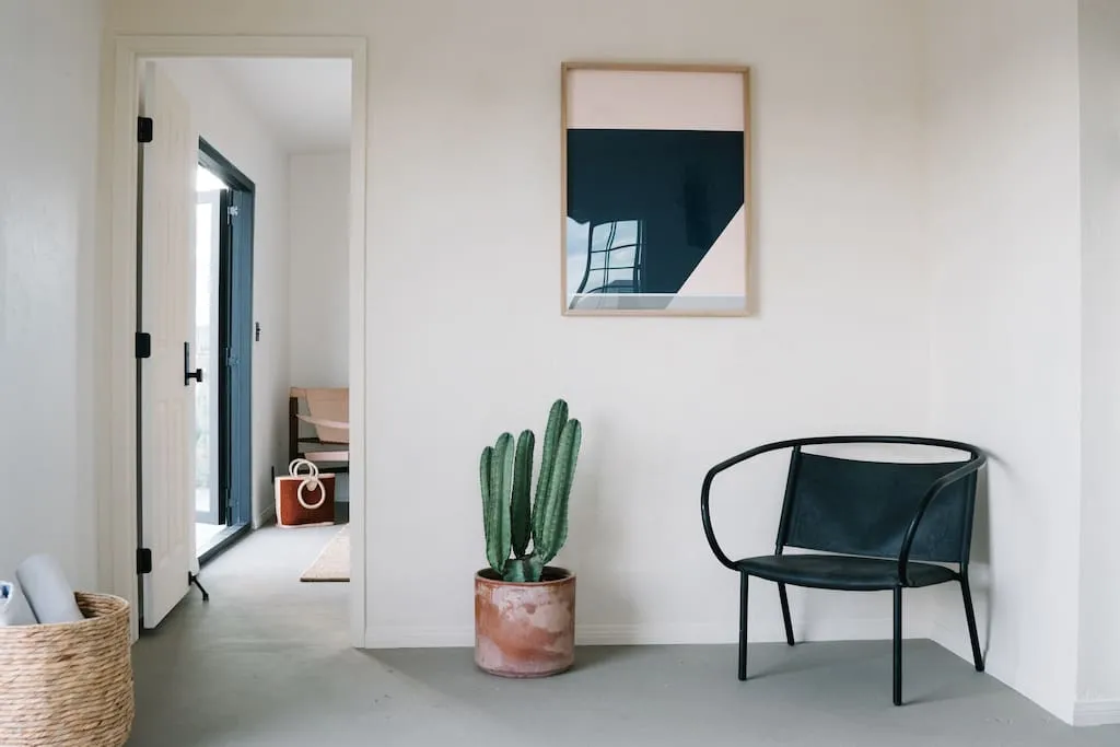 A modern, minimalist interior design featuring concrete elements, a black chair, a cactus plant, and a framed abstract art pi