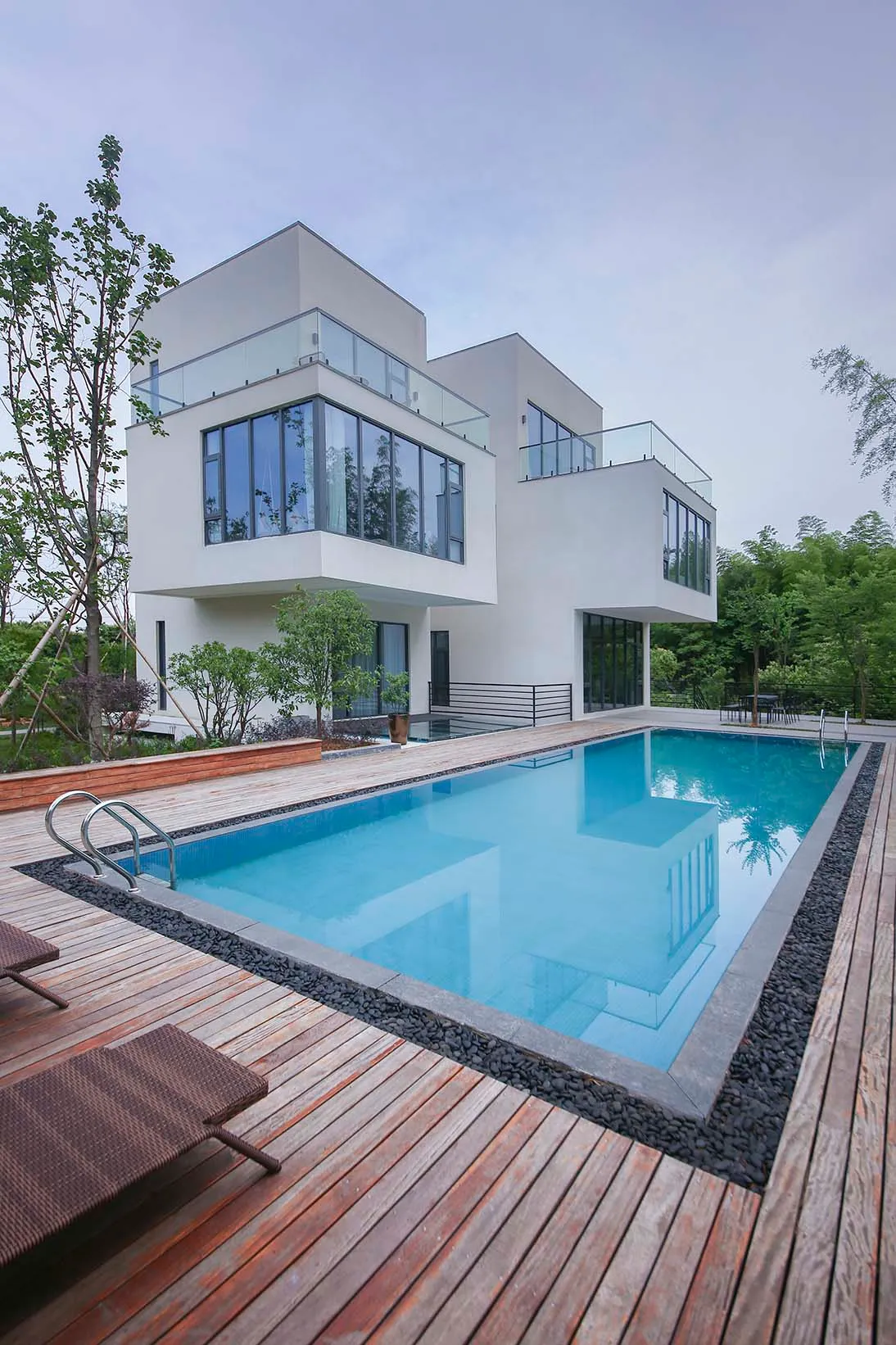 Modern house exterior featuring a white concrete and glass structure with a wooden deck and a swimming pool.
