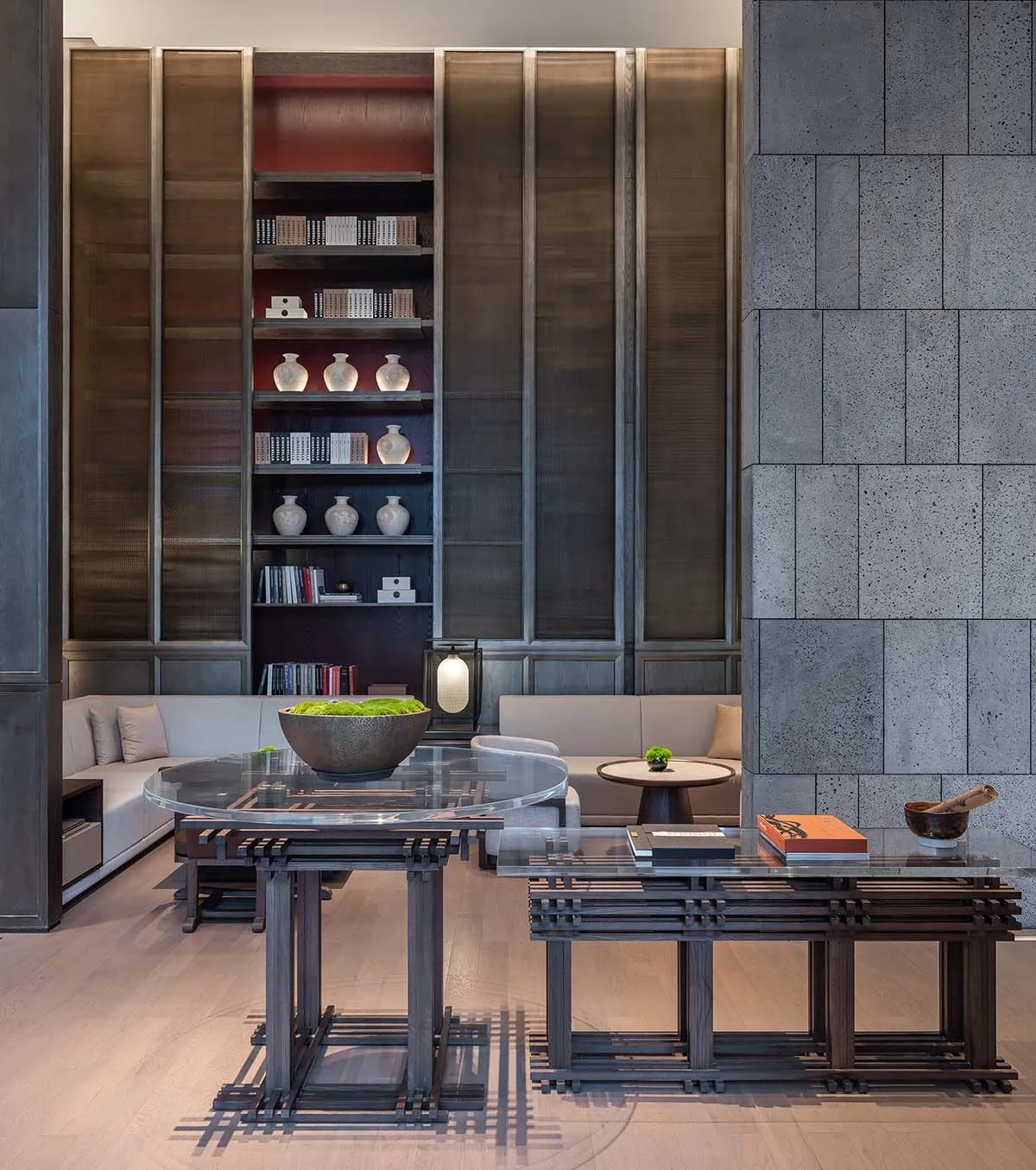 A modern living room featuring wooden furniture, concrete walls, and glass tables
