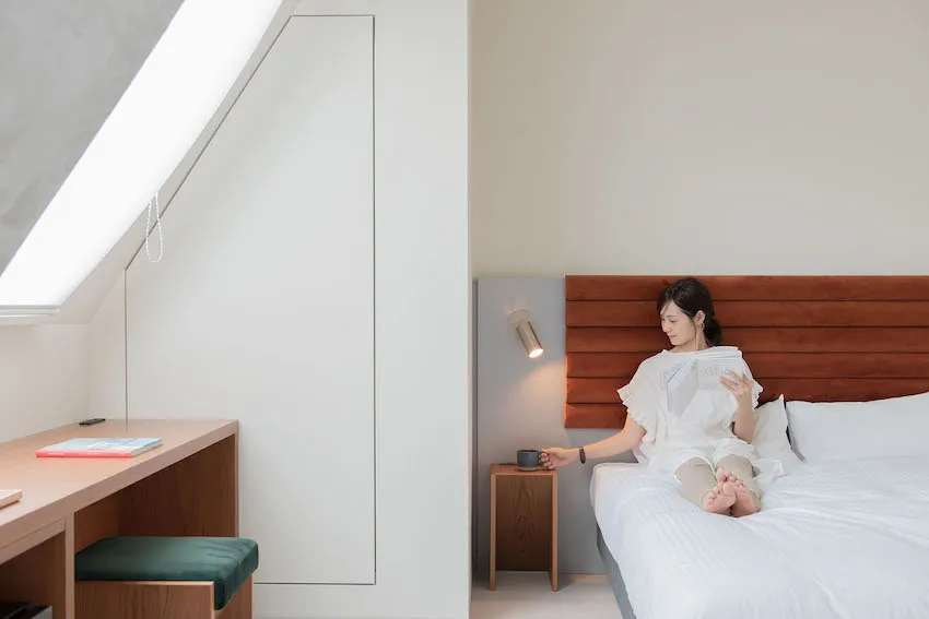 A woman sits on a modern minimalist white bed in a bedroom.