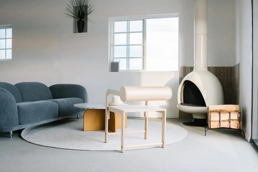 A modern minimalist living room with a blue sofa, round coffee table, and white fireplace.
