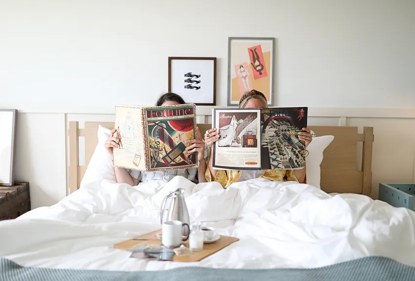 Two individuals laying in bed with open magazines in front of them.