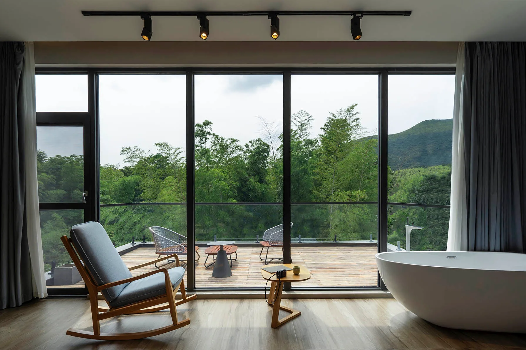 A minimalist interior with an outdoor seating area on a wooden deck overlooking lush greenery.