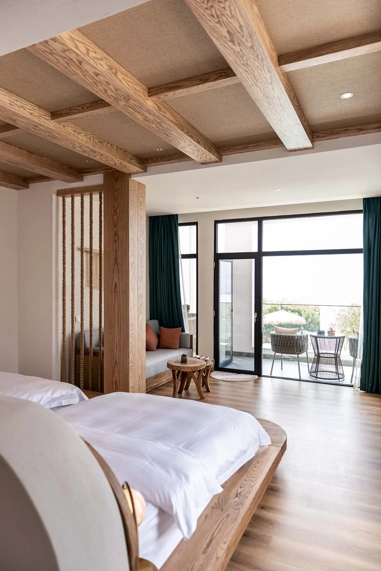 Modern bedroom with a white bed, wooden furniture, and a view of a balcony with chairs and a table.