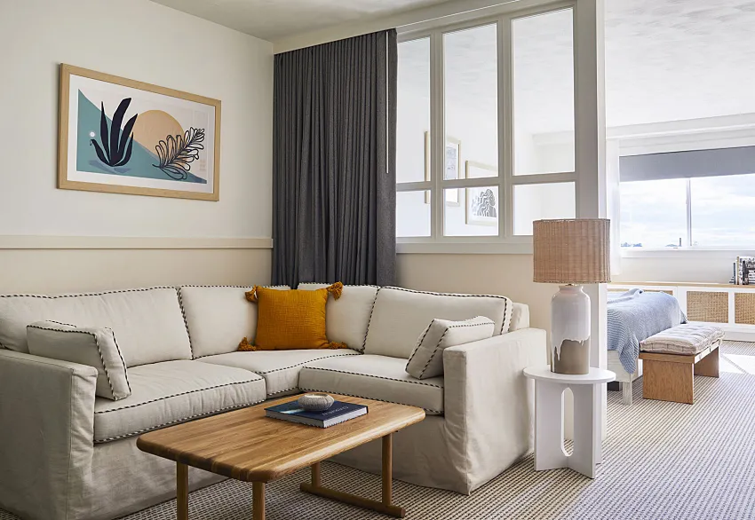A modern living room with a white sectional sofa, wooden coffee table, and large windows.