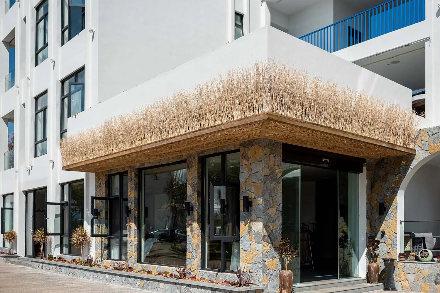 Modern residential entrance featuring stone materials, glass doors, and a thatched rooftop awning.