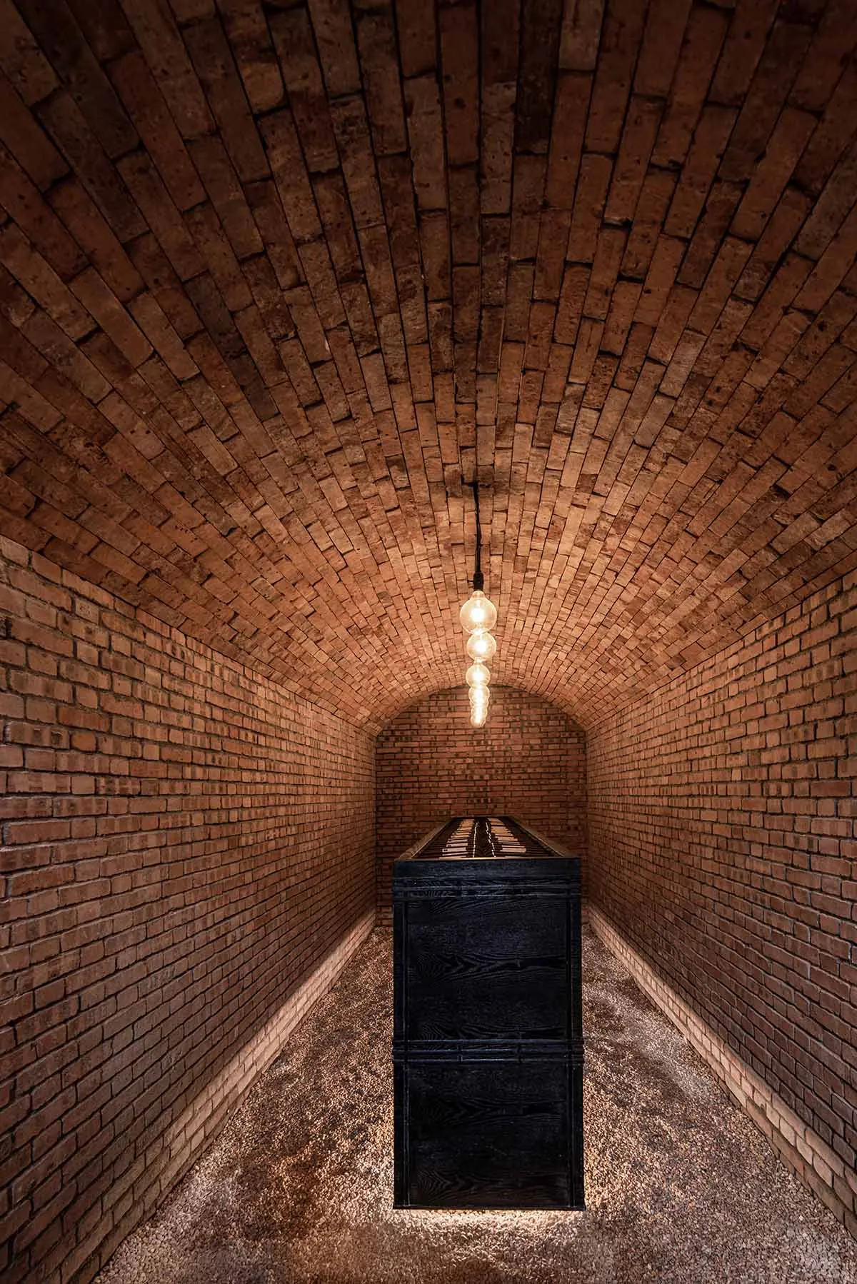 Industrial brick corridor with wooden box, illuminated by hanging light bulbs.