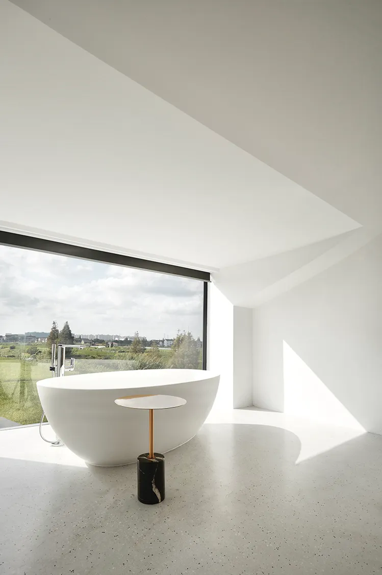 A minimalist bathroom with a freestanding white bathtub, a black and white marble table, and a large window with a view of th