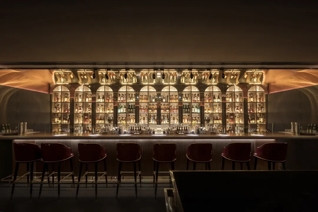 A modern bar with metal-clad shelves filled with bottles of alcohol and seating for patrons.