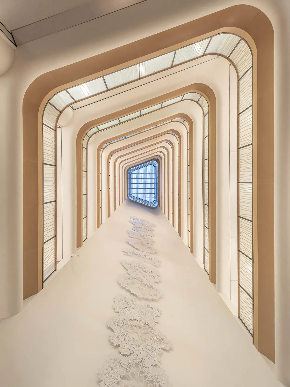 A modern corridor with glass walls and a concrete floor, featuring a geometric design.