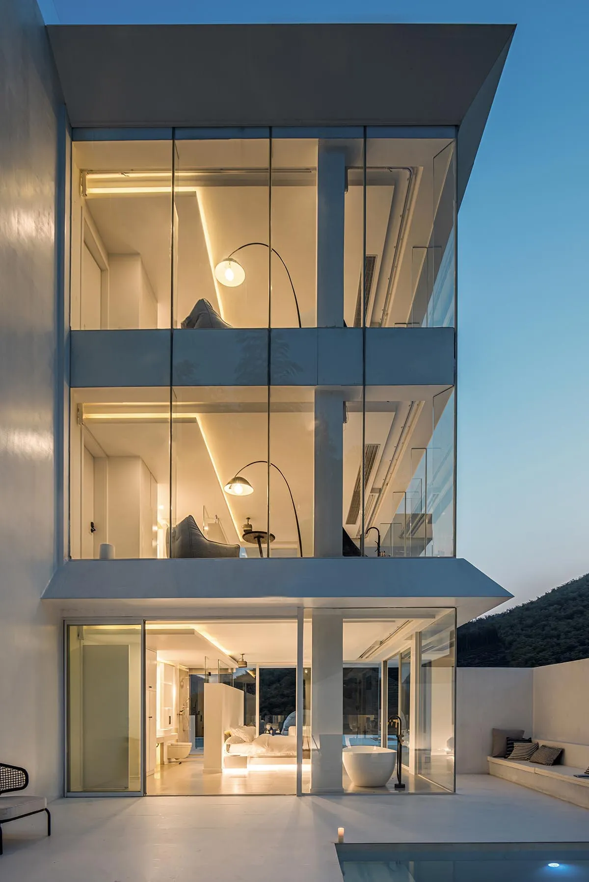 A modern glass house with a minimalist design, illuminated at night, showcasing cozy lighting and a serene atmosphere.