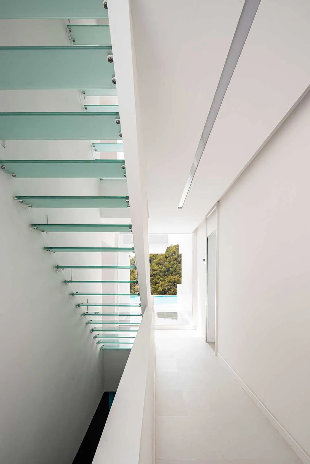 A modern interior with glass and concrete staircase leading to a bright, airy space.