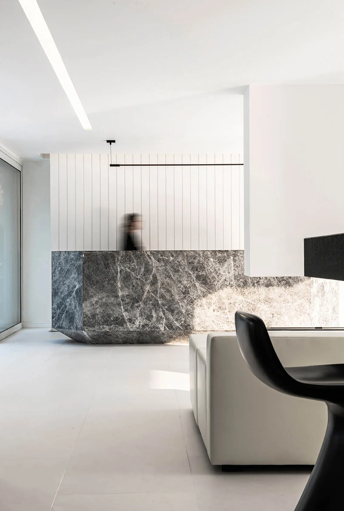 A modern lobby featuring a large marble reception desk and white seating area.