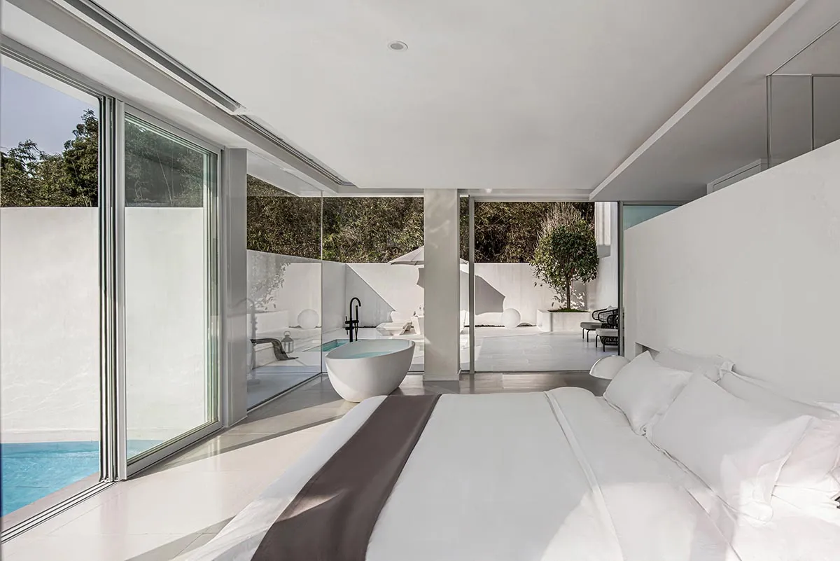 Modern minimalist bedroom with glass walls and white surfaces.
