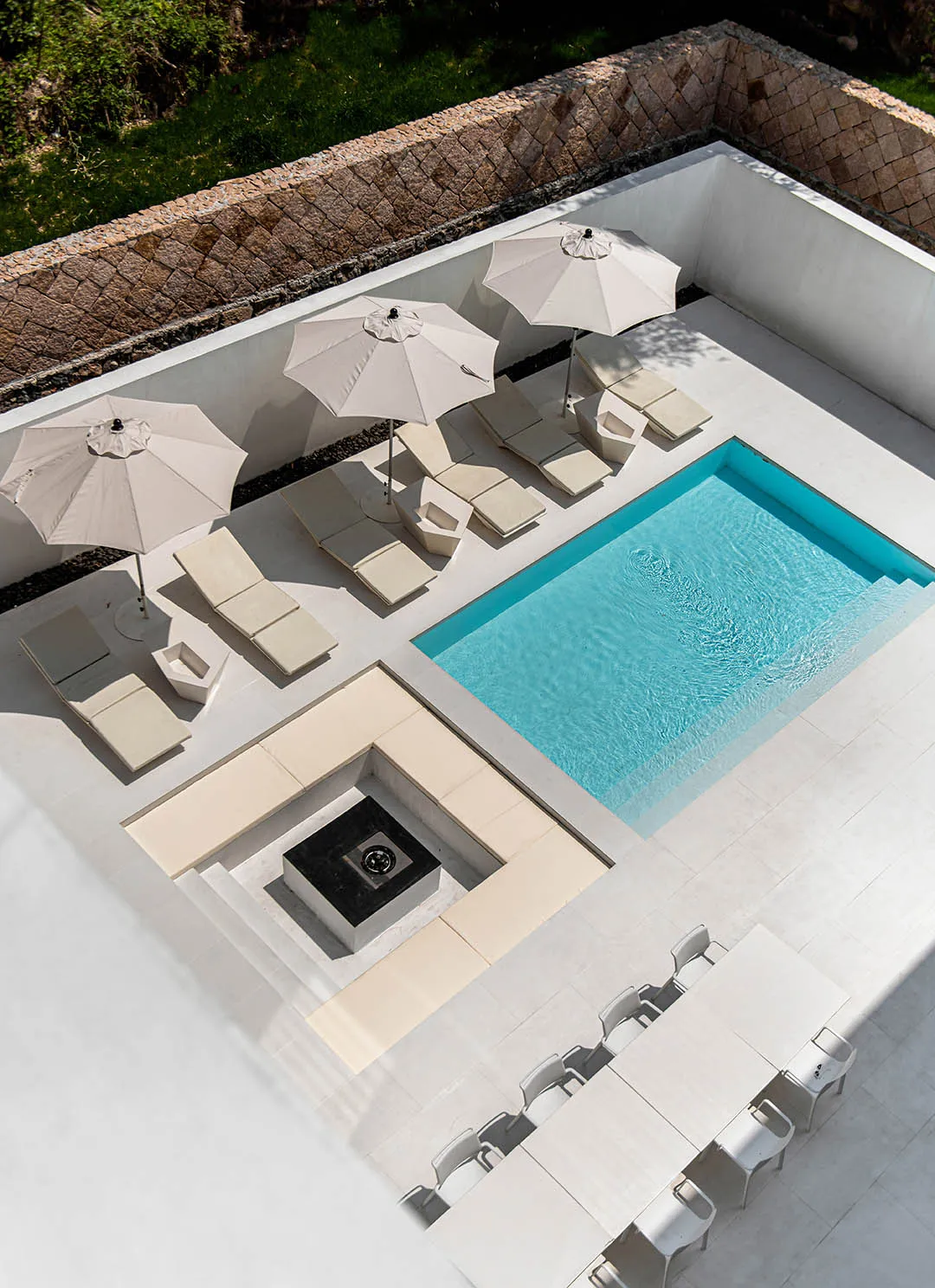 A modern outdoor living area featuring a rectangular pool with turquoise water, surrounded by white umbrellas, beige lounge c
