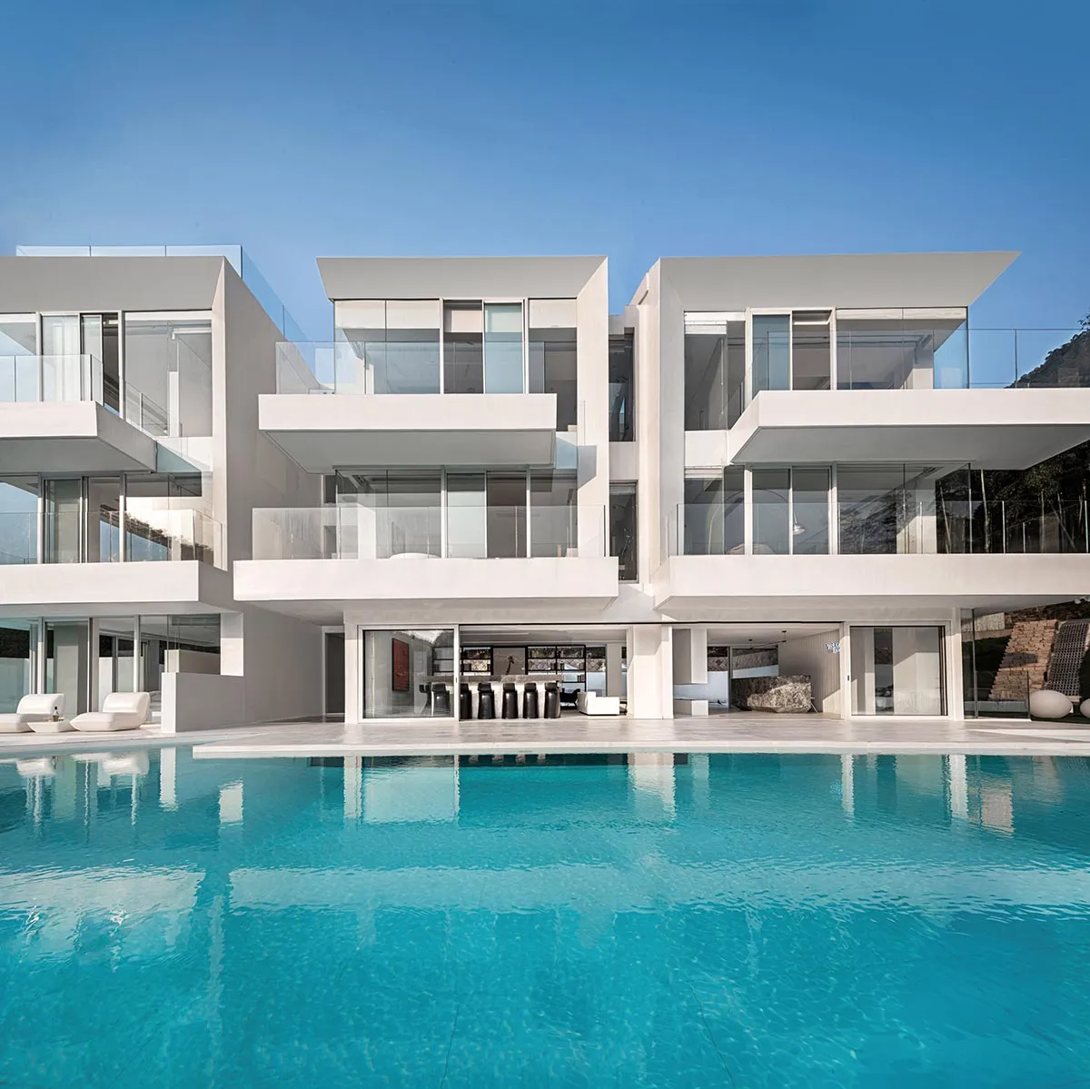 A modern residential pool house featuring white stone and glass exterior materials.