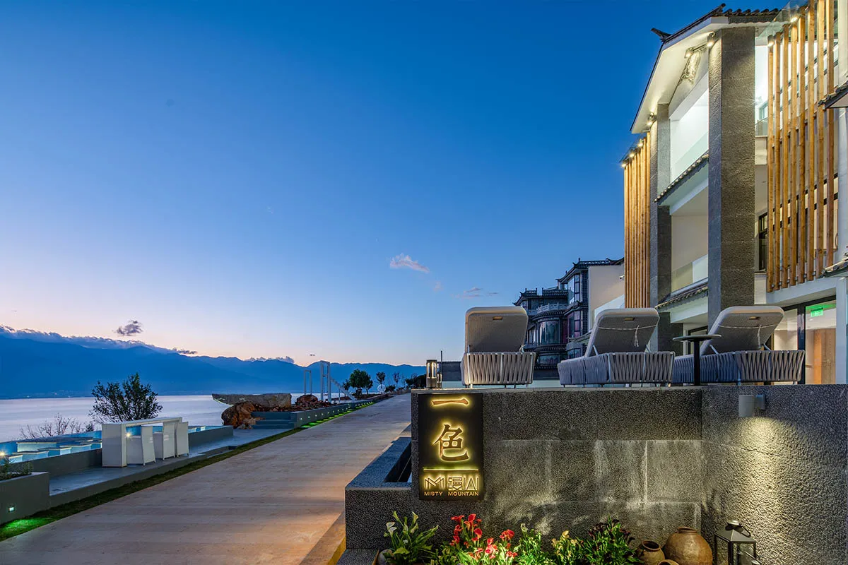 An evening view of a modern resort featuring a building with a prominent contemporary design, illuminated exterior lights, an