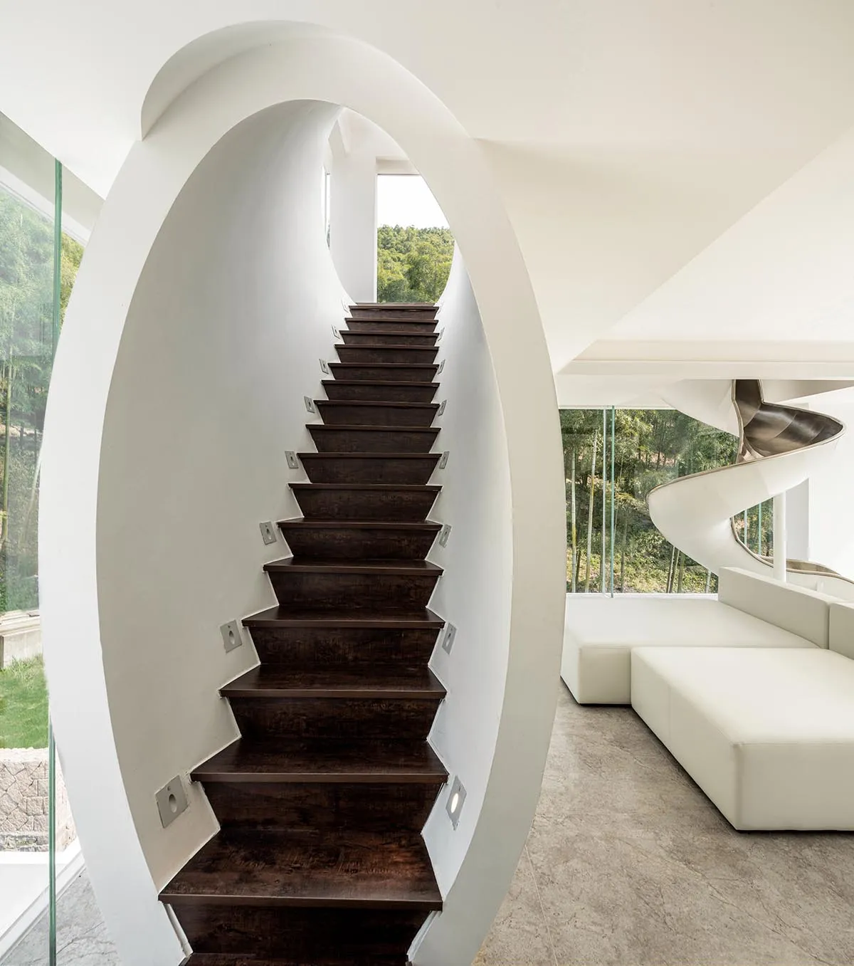A modern interior featuring dark wooden stairs with white walls and floors.