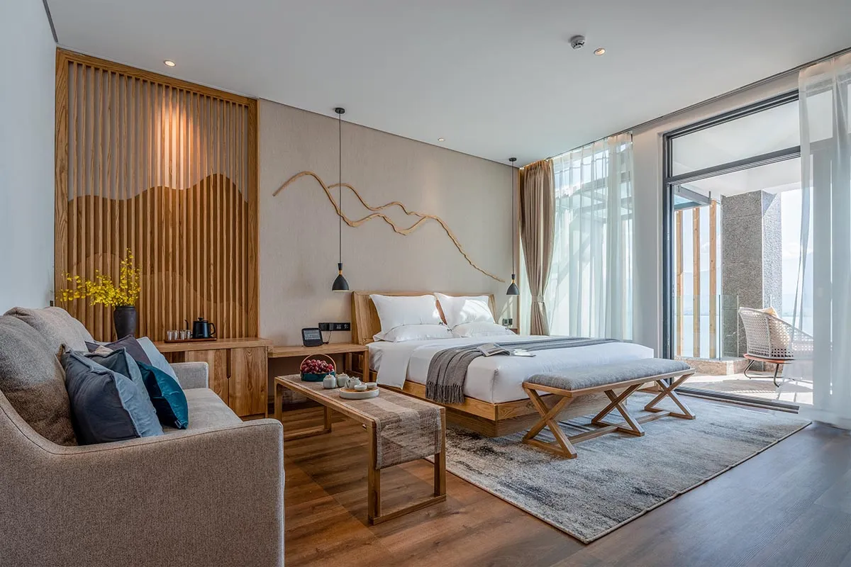 Modern bedroom featuring a wooden bed frame, white linens, and a textured rug, with a cozy armchair and wooden accents.