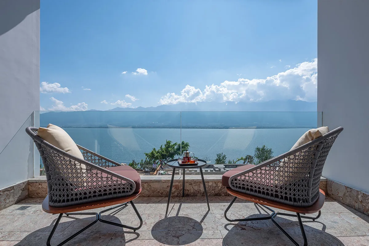 Two modern patio chairs with cushions and a small table with tea set, overlooking a vast ocean under a clear blue sky with sc