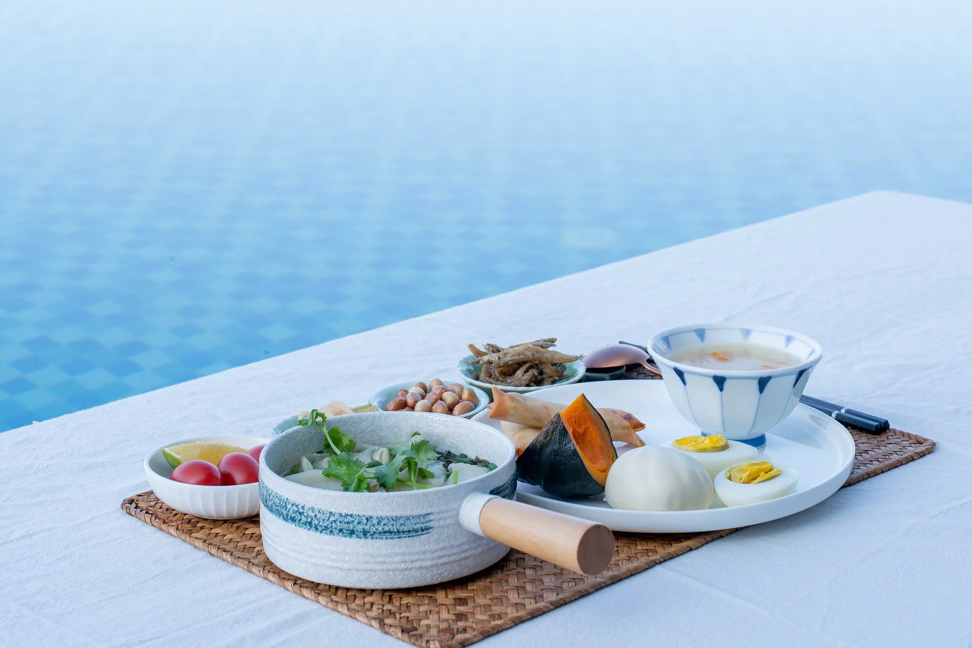 A table setting featuring a variety of dishes served on ceramic plates near a swimming pool.