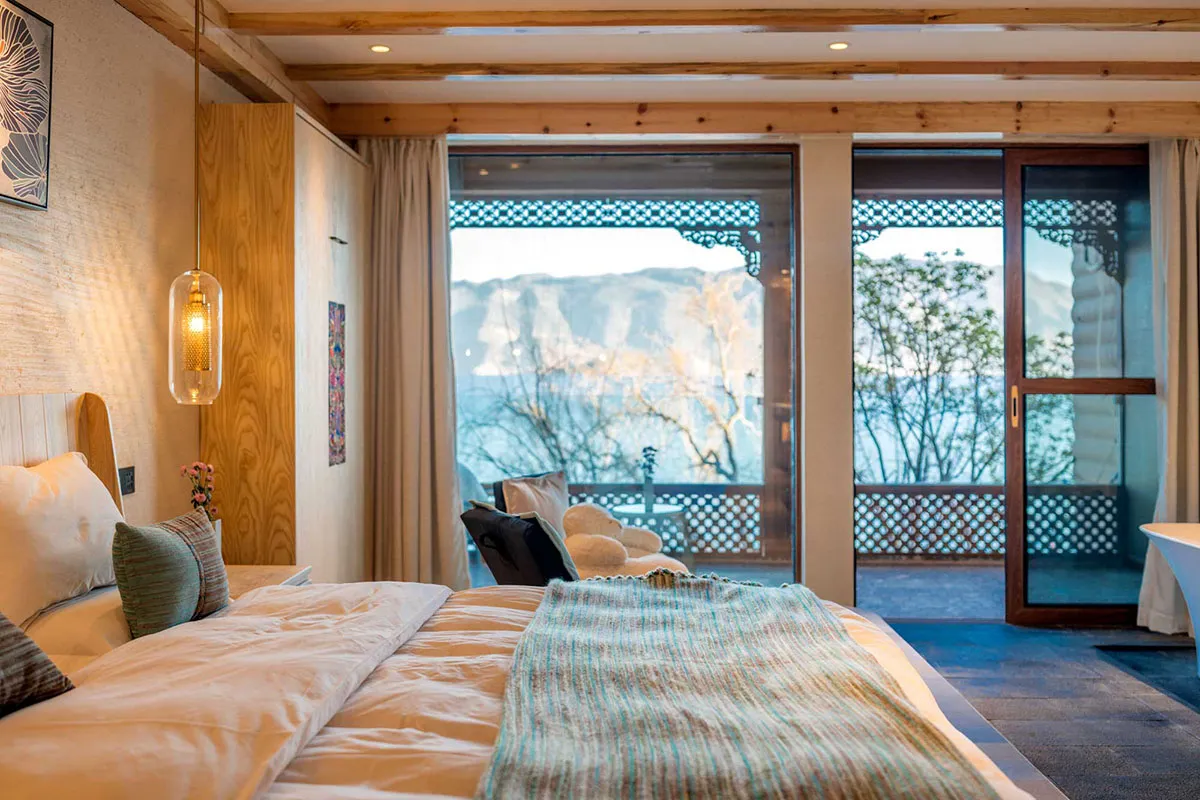 A modern bedroom with wooden walls, glass doors, and soft textiles on the bed.