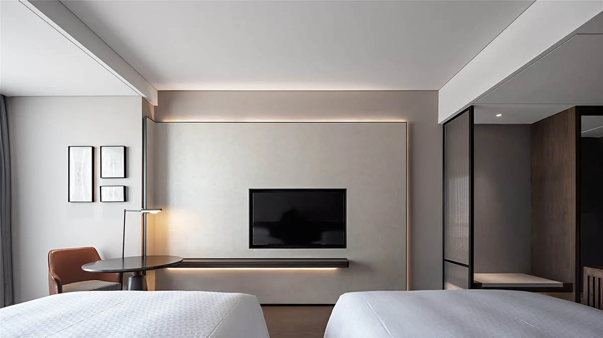 A minimalist bedroom with a modern aesthetic, featuring white beds, a TV mounted on the wall, and a floor lamp.