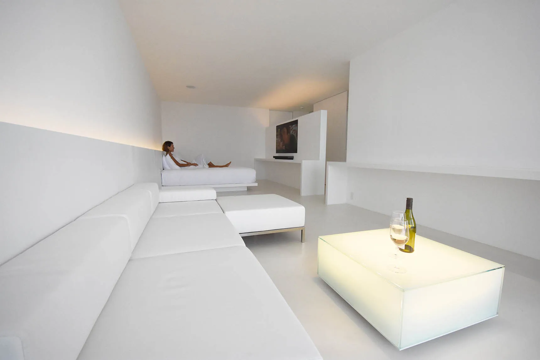 A minimalist living room with white furniture and concrete walls and floor